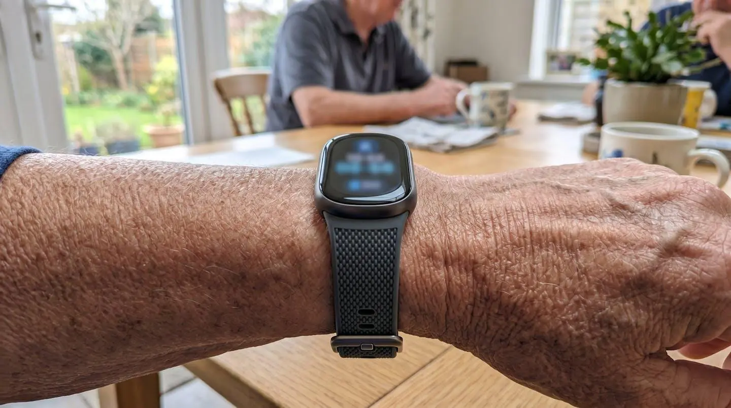 Gros plan sur un bracelet de télésurveillance médical moderne au poignet d'une personne âgée, focus net sur le dispositif, arrière-plan flouté avec vêtement et bras